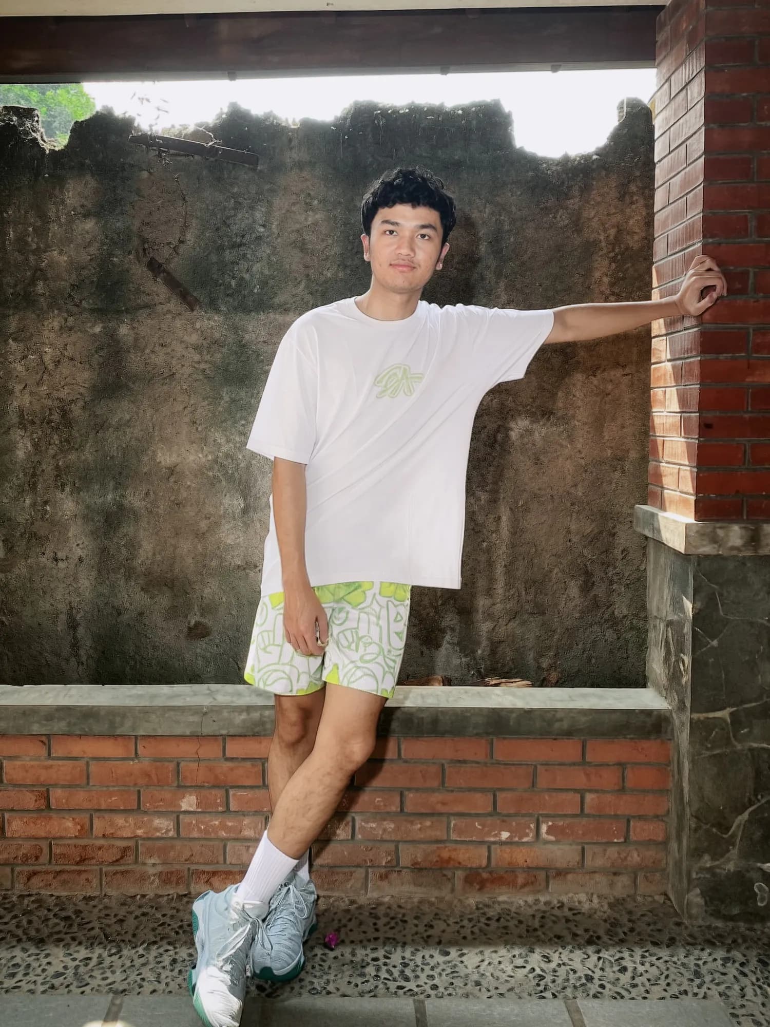Lime Urban Doodle Shortpants shorts and a white tee with a lime BA logo, worn leaning on a brick pillar by a mossy wall.