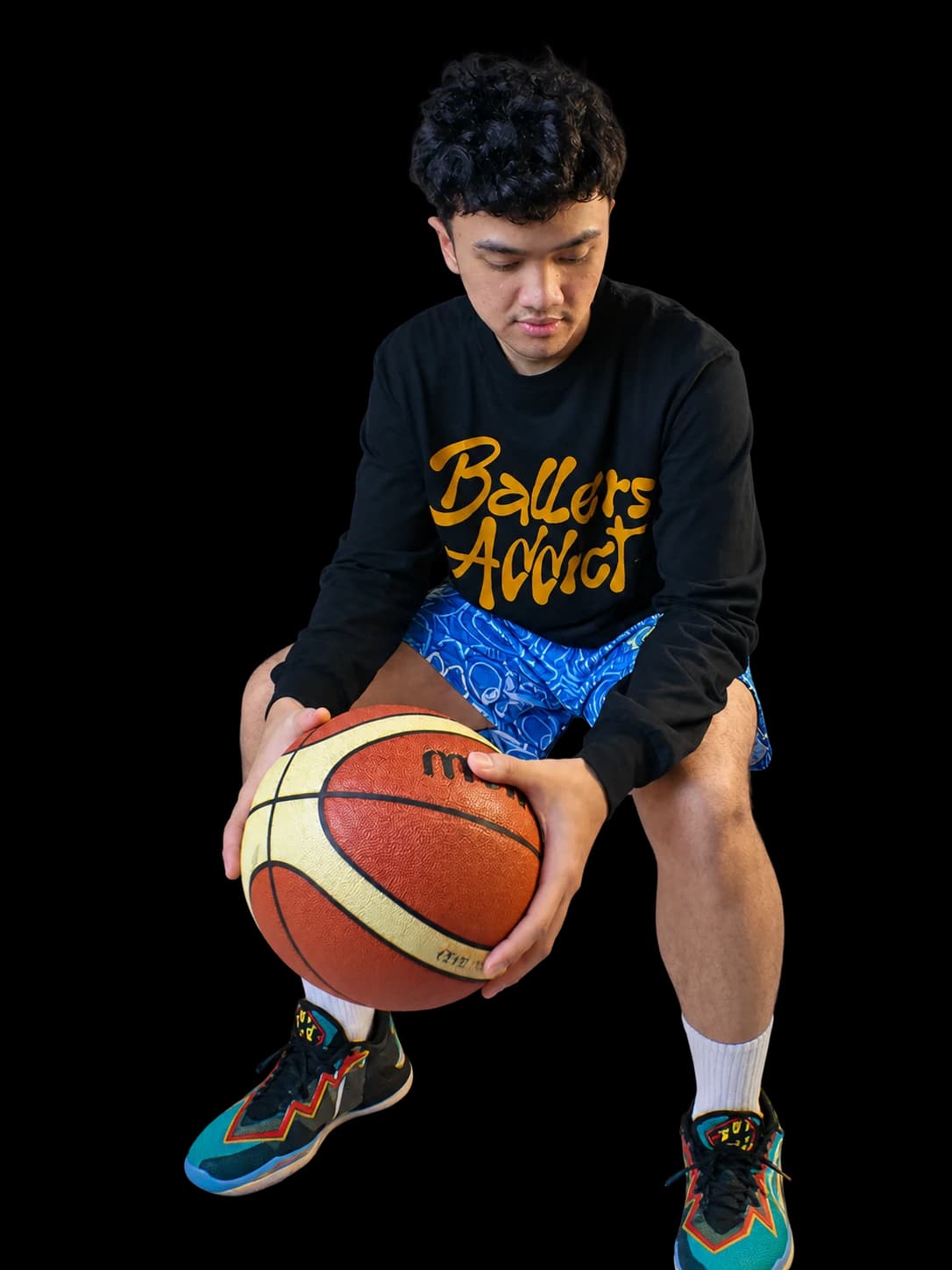 Blue Urban Doodle Shortpants shorts and a black long-sleeve with a mustard Ballers Addict script, crouching with a basketball.