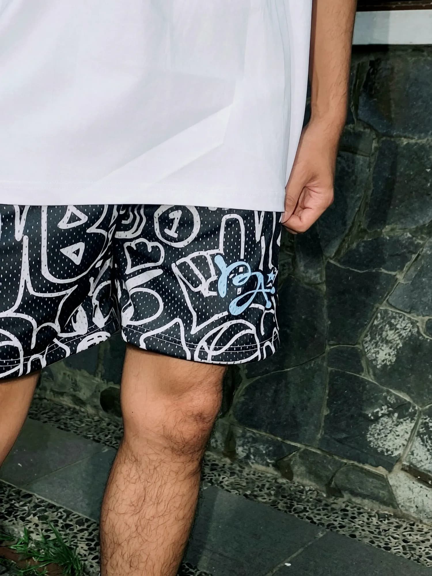 Close-up of the Black Urban Doodle Shortpants shorts: black mesh, white line work and a light-blue BA monogram under a white tee.