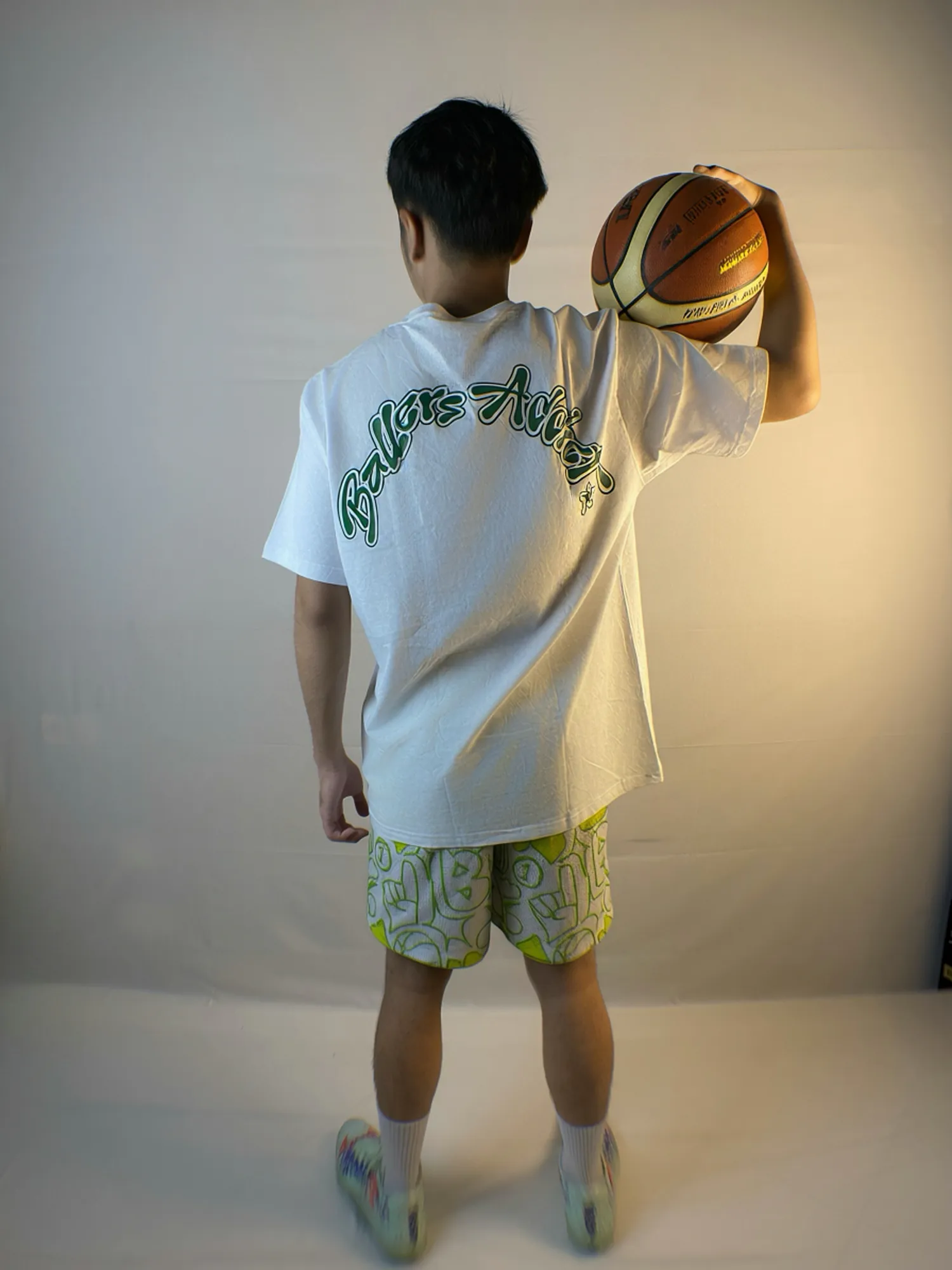 Lime Urban Doodle Shortpants shorts and a white tee with a green Ballers Addict back print, seen from behind with a basketball on the shoulder.