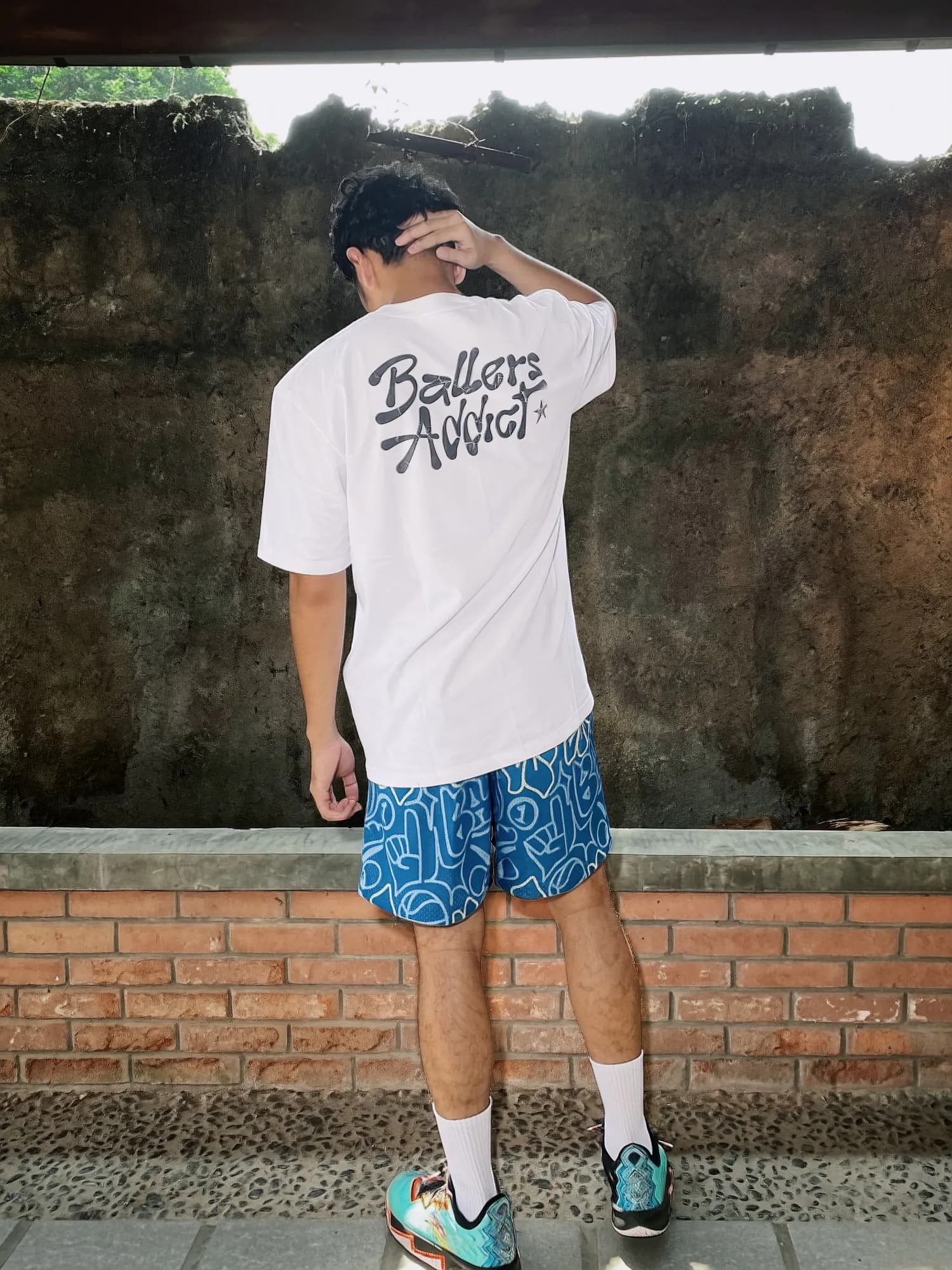 Blue Urban Doodle Shortpants shorts and a white tee with a black Ballers Addict back print, seen from behind with a hand on the head.